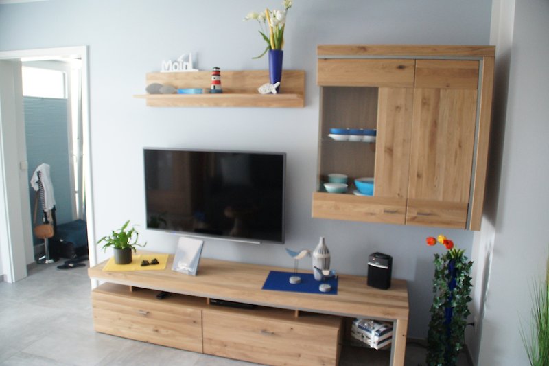 Wohnzimmer mit Holzwänden, Fernseher, Blumen und Regal.
