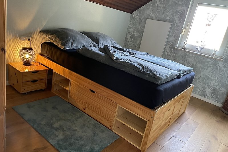 Komfortables Schlafzimmer mit Holzbett, Fenster und Nachttisch.