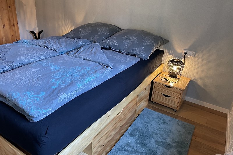 Gemütliches Schlafzimmer mit Holzbett und Nachttisch. Gemütliche Beleuchtung.