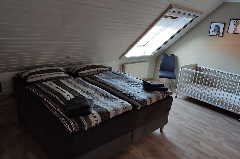 Schlafzimmer mit Holzbett, Fenster und Bettwäsche.
