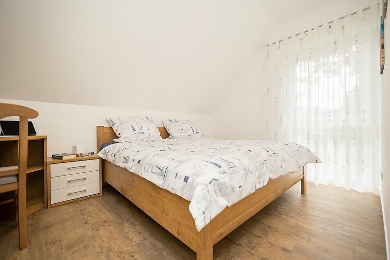 Schlafzimmer mit bequemem Bett, Holzmöbeln und Fenster.