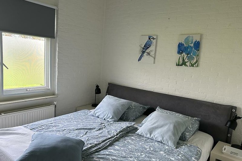 Schlafzimmer mit Doppelbett, blauer Bettwäsche, Kunst und Lampen. Gemütlich und stilvoll.