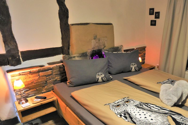 Gemütliches Schlafzimmer mit lila Bettwäsche, Holzrahmen und Nachttischlampe. Gemütliche Atmosphäre!