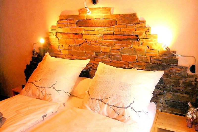 Schlafzimmer mit orangefarbener Bettwäsche, Holzrahmen und gemütlicher Beleuchtung.