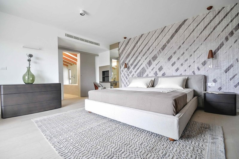 Stilvolles Schlafzimmer mit grauer Wand, gemütlichem Bett und Lampen.
