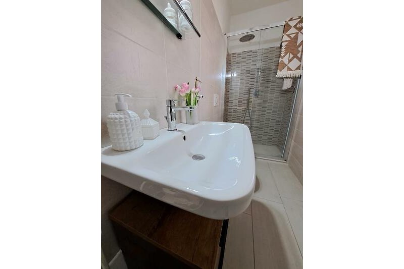 Modernes Badezimmer mit rechteckigem Spiegel und Pflanze.