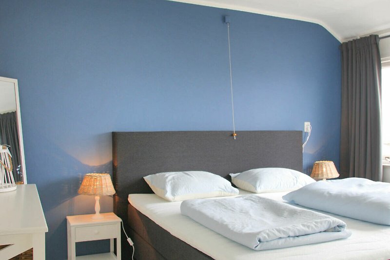 Schlafzimmer mit Bett, Kissen, Lampe und Vorhängen.