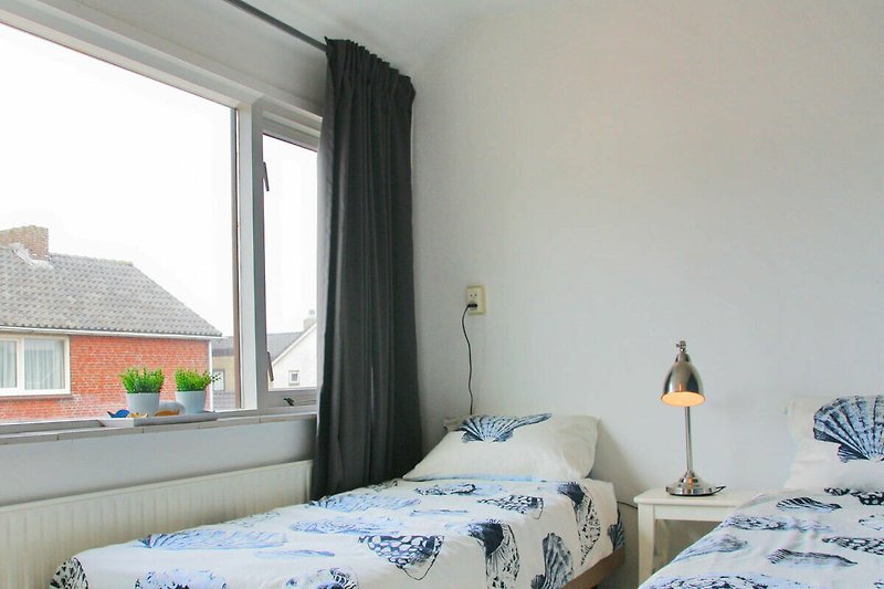 Schlafzimmer mit gemütlichem Bett, Fenster und Vorhängen.