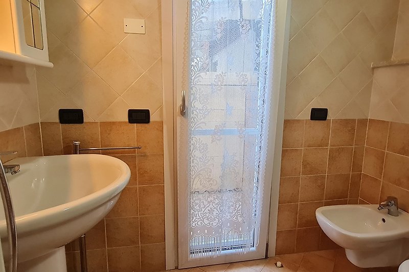 Badezimmer mit Keramikwaschbecken, Badewanne und Fenster.