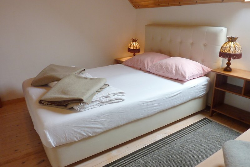 Schlafzimmer mit gemütlichem Bett, Holzmöbeln und Lampen.