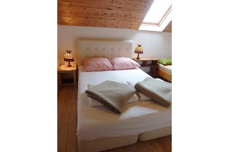 Schlafzimmer mit Holzmöbeln, Bett, Kissen und Lampe.