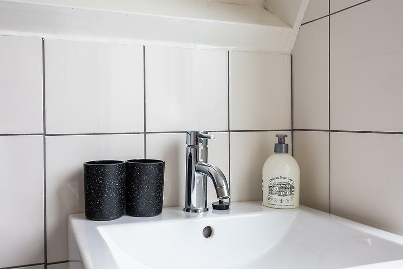 Modernes Badezimmer mit grauer Keramik und Glasflasche.