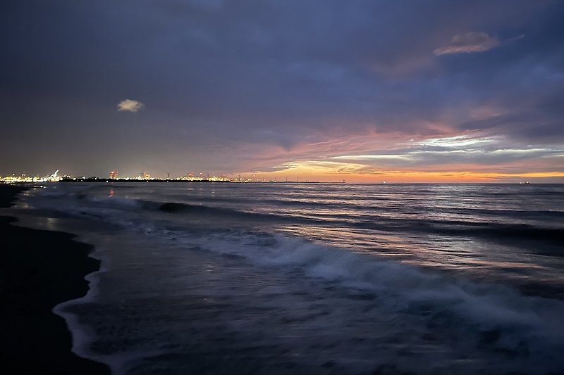 Strand mit Sonnenuntergang, Wellen und Felsen.