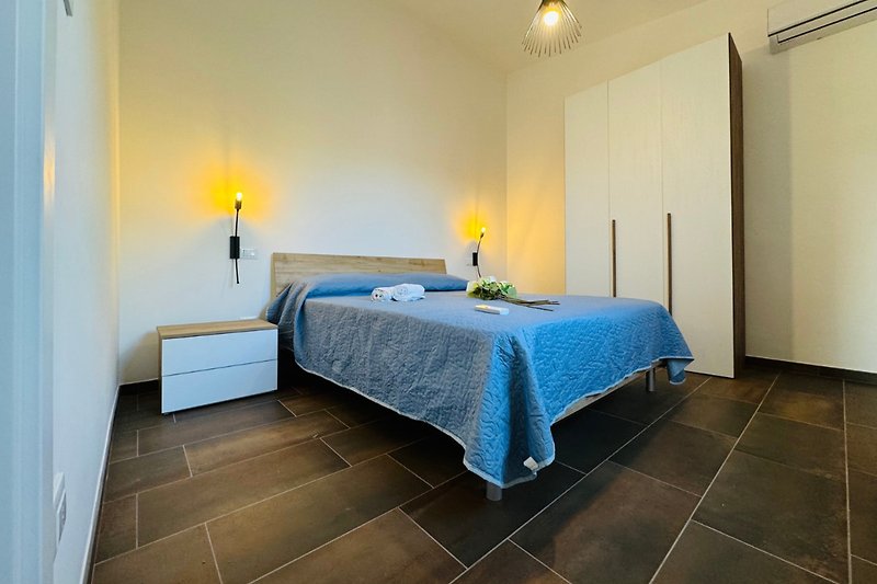 Schlafzimmer mit blauer Bettwäsche, Holzmöbeln und Lampen.