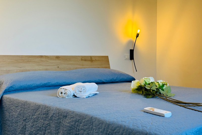 Schlafzimmer mit blauer Bettwäsche, Lampen und Blumen.