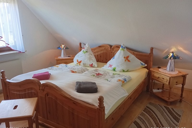 Schlafzimmer 1 mit Holzmöbeln, Bettwäsche und Vorhängen.