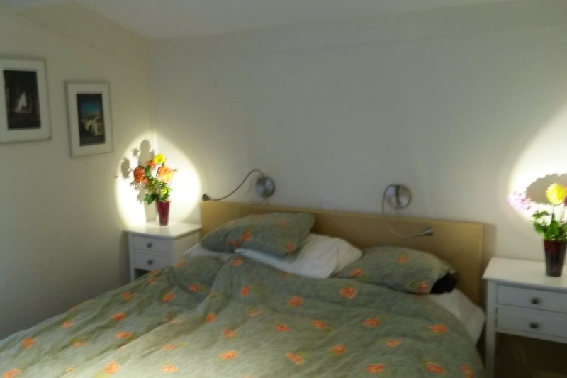 Schlafzimmer mit gemütlichem Bett, stilvoller Beleuchtung und Blumen.