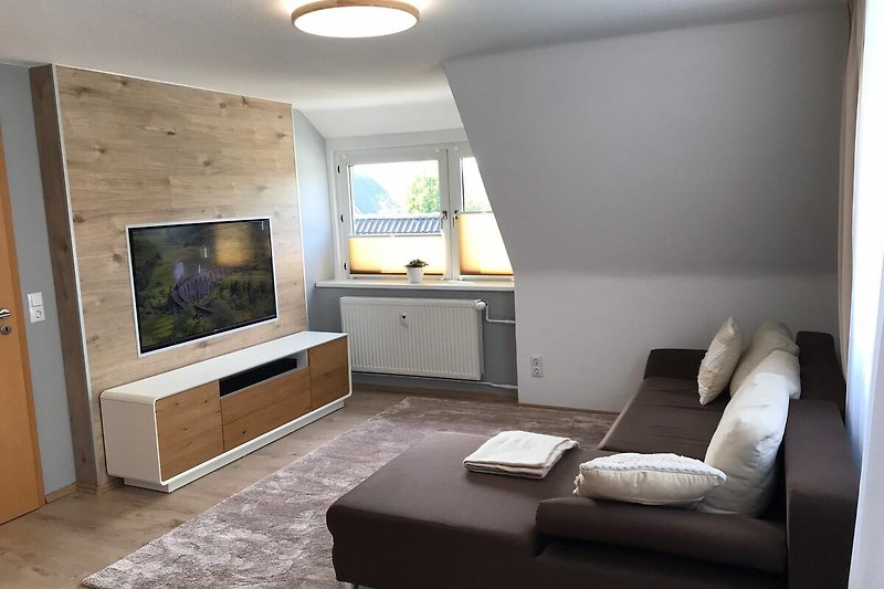 Modernes Wohnzimmer mit TV, Holzmöbeln und gemütlichem Ambiente.