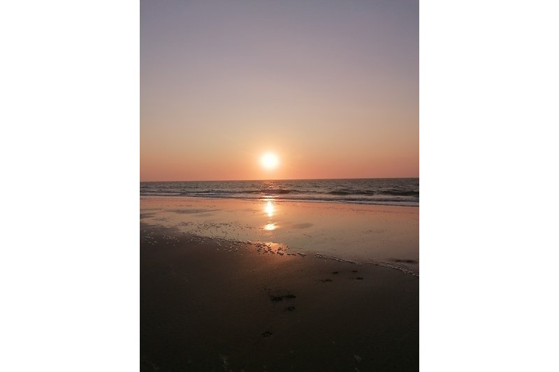 Strand mit ruhigem Meer, rotem Sonnenuntergang.