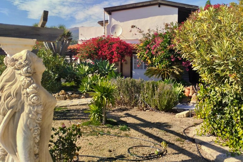 Klassische Skulptur im Garten mit blühenden Pflanzen