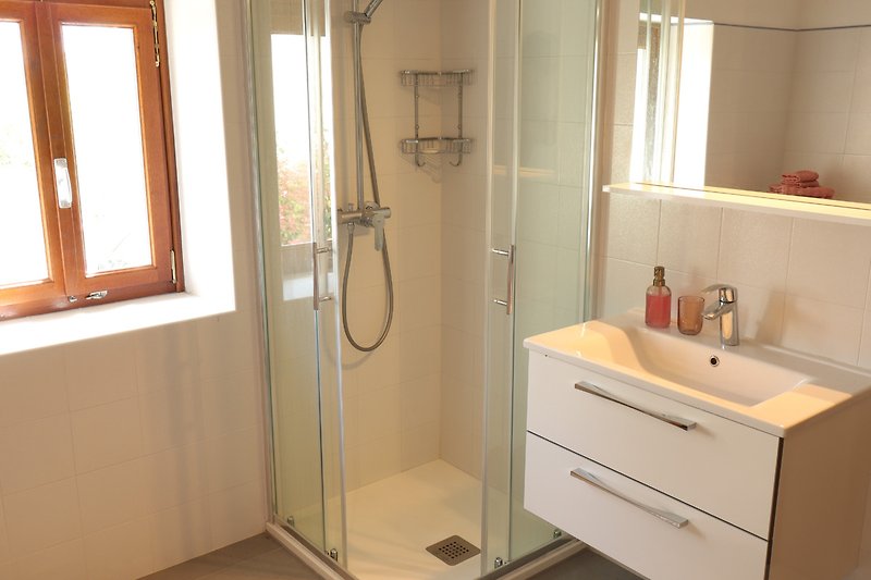Modernes Badezimmer mit Glasdusche, Spiegel und Armatur.