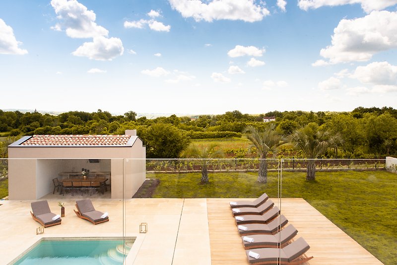 Modernes Haus mit Pool, grünem Garten und blauem Himmel.