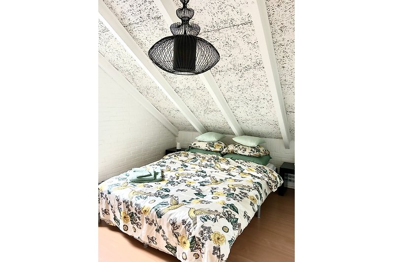 Gemütliches Schlafzimmer mit Bett, Kissen, Holzdecke und Lampe.