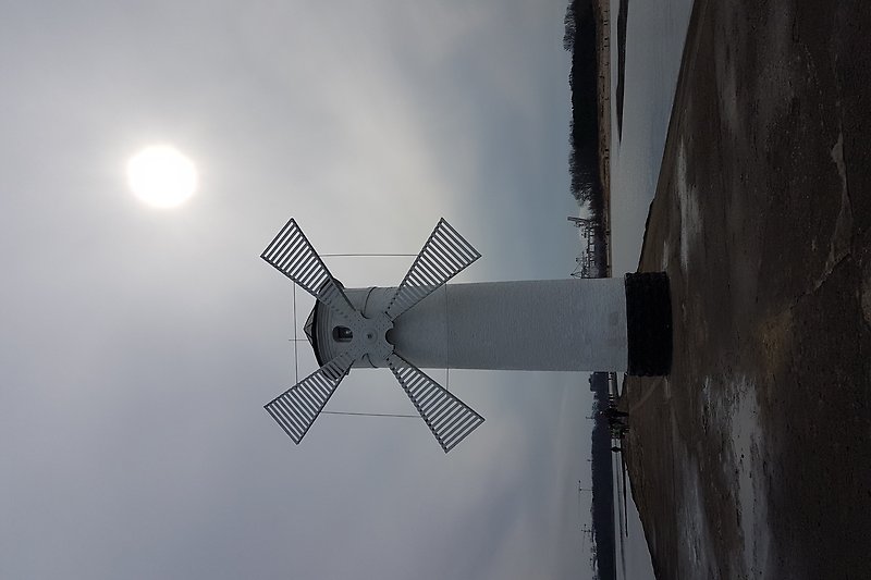 Windmühle mit Turbine und Flutlicht am Wasser.
