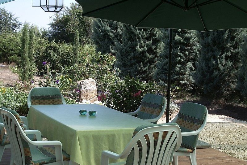 Garten mit Tisch, Stühlen, Sonnenschirm und Blumen.