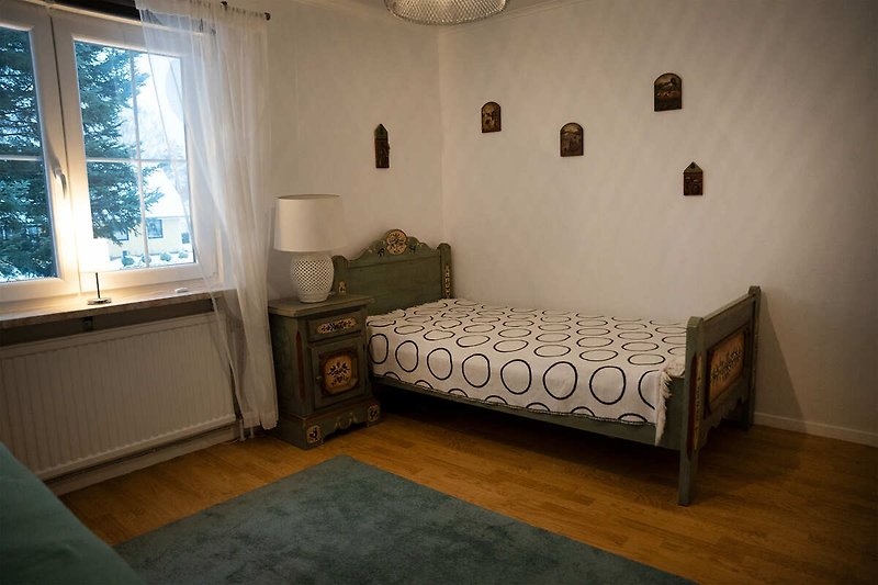 Schlafzimmer mit gemütlichem Bett, Fenster und Kunst.
