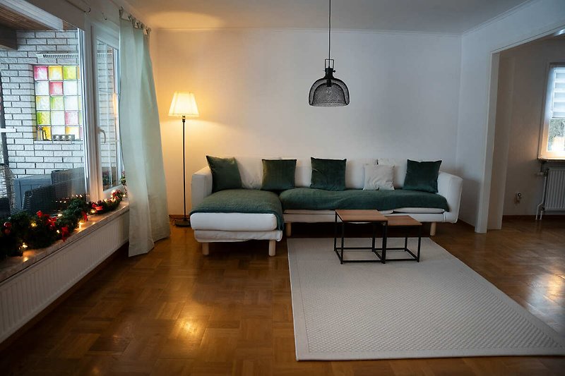 Wohnzimmer mit grauem Sofa, Holztisch und Lampen.