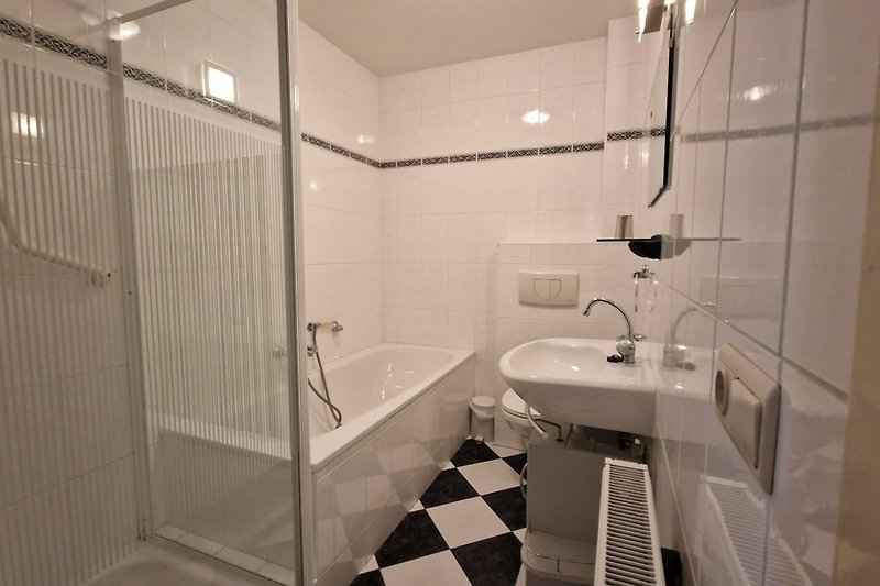 Badezimmer mit Dusche, Badewanne, Spiegel und Pflanze.