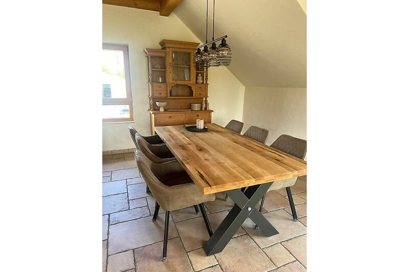 Ein helles Wohnzimmer mit Holzmöbeln, Tisch, Stuhl und Lampe.