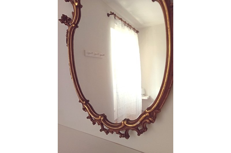 Spiegel mit Kupferkette und Schmuck in ovalem Rahmen.