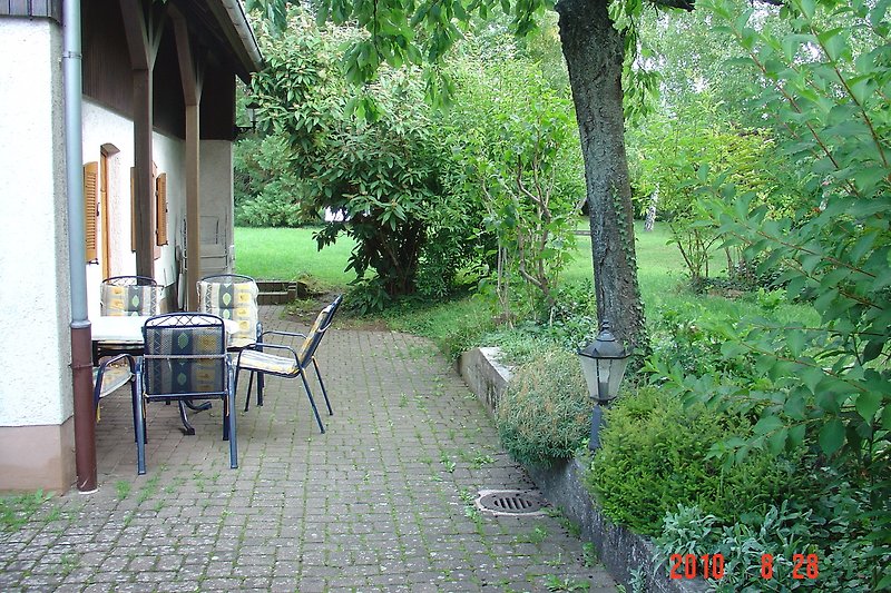 Gartenidylle mit Haus, Tisch und Stühlen.