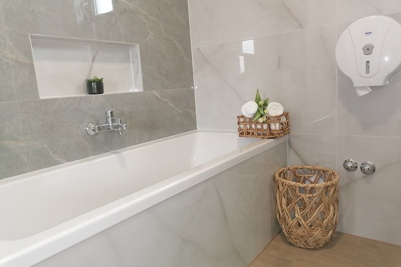 Badezimmer mit Spiegel, Badewanne und Pflanze.