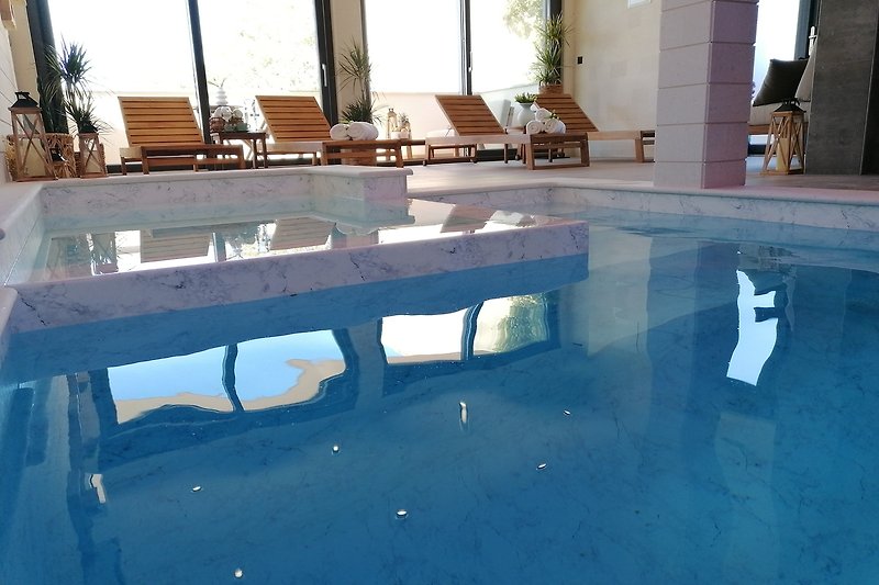 Schwimmbad mit Holzdeck und Glasfassade.