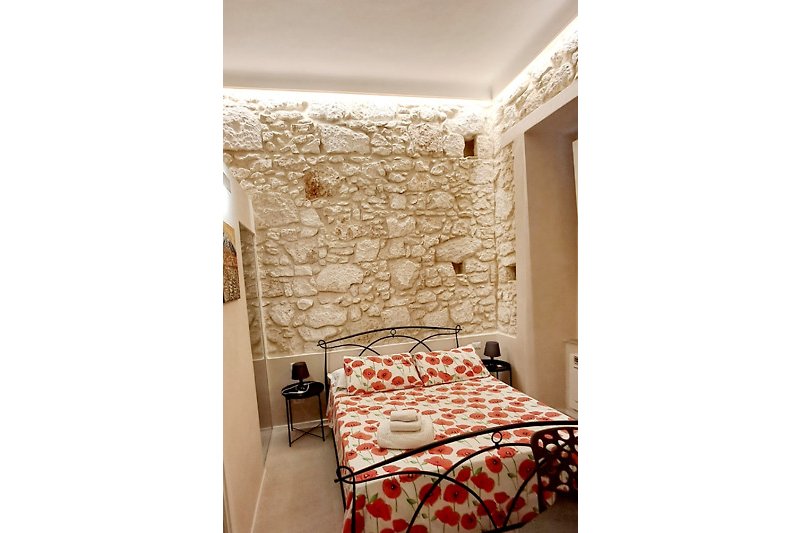 Modernes Schlafzimmer mit Holzbett und Metallstuhl. Gemütliche Bettwäsche in Pfirsichfarbe.
