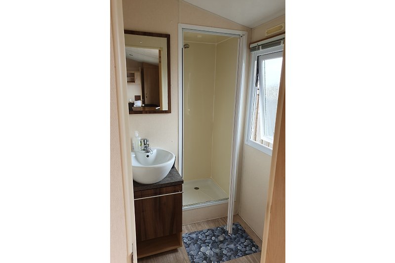 Badezimmer mit Spiegel, Waschbecken, Dusche und Badmöbel