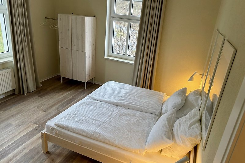 Schlafzimmer mit Holzmöbeln, gemütlichem Bett und Vorhängen.
