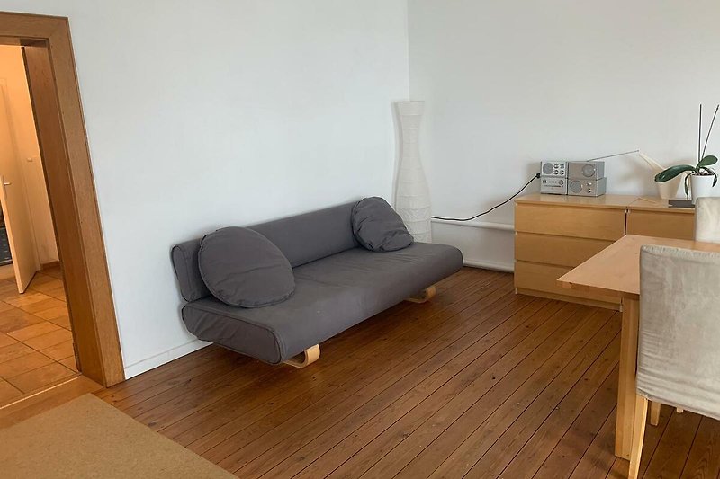 Wohnzimmer mit bequemer Couch, Holztisch und Pflanze.