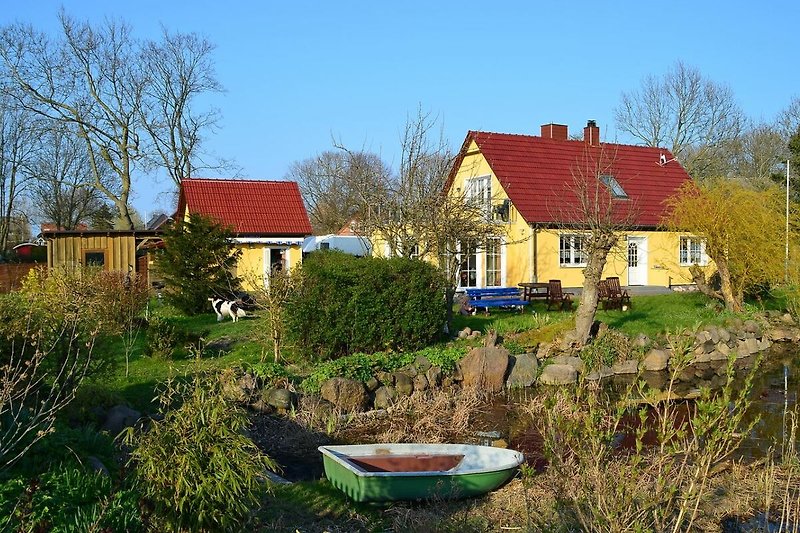 Ländliches Haus mit Boot am Wasser und grüner Landschaft.