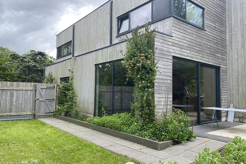 Gemütlicher Garten mit Bäumen, Rasen und Holzfassade.