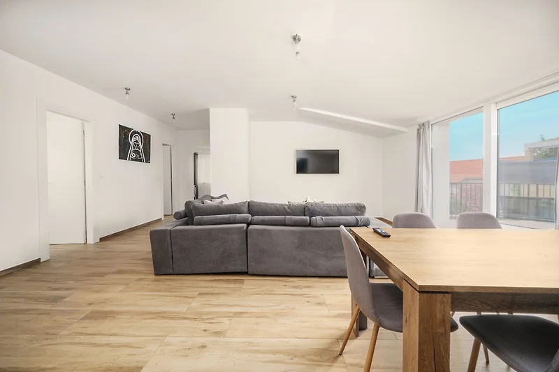 Wohnzimmer mit Holzdecke, Esstisch, Tageslicht und bequemer Couch.