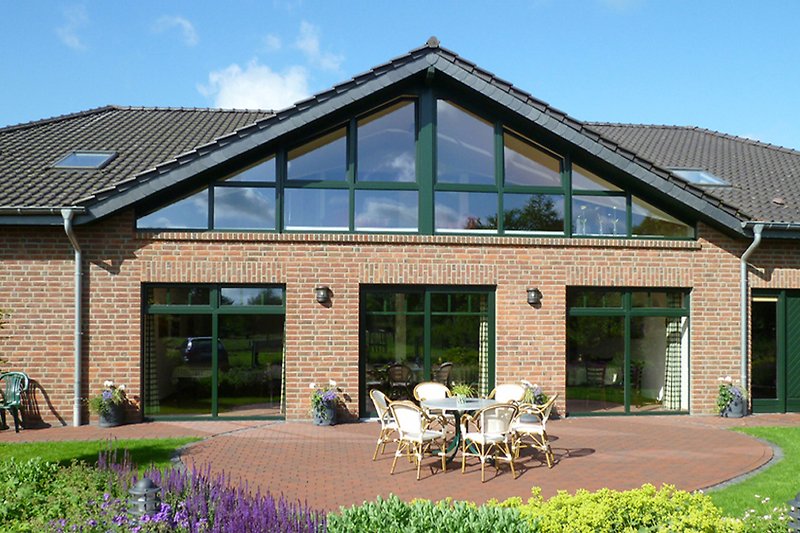 Charmantes Haus mit Garten, Veranda und blühenden Blumen.