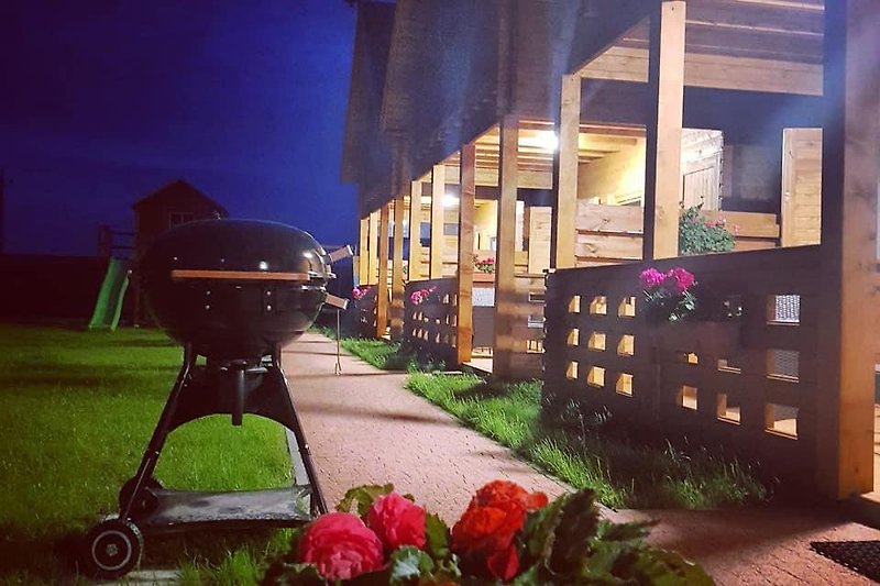 Blühender Garten mit Rosen, Rasen und beleuchtetem Haus bei Nacht.