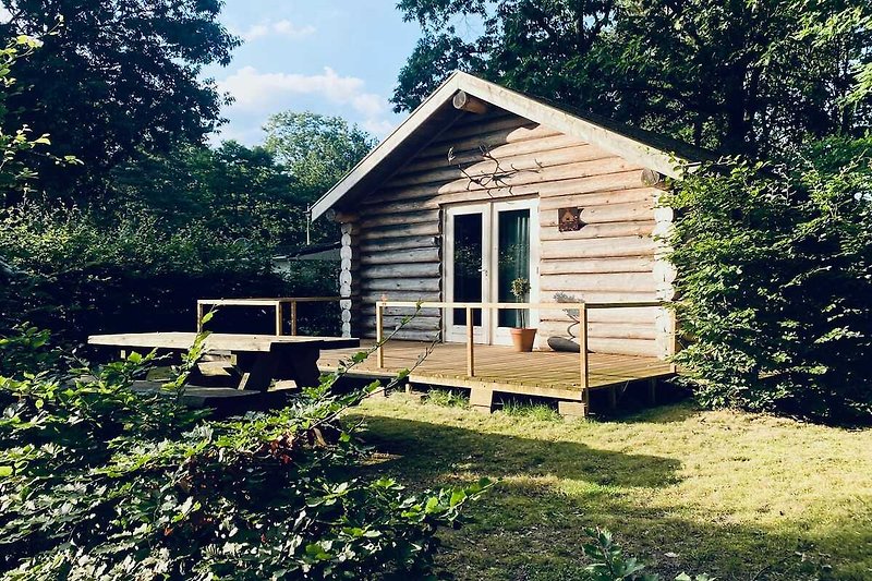 Gemütliches Holzhaus mit Garten, Bäumen und blauem Himmel.