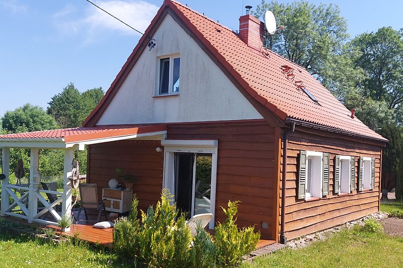 Charmantes Landhaus mit Garten, Holzveranda und blühenden Blumen.