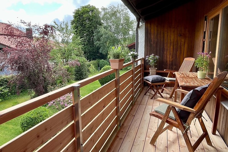 Geräumiger Balkon mit Pflanzen, Holzstühlen und Tisch zum Essen.