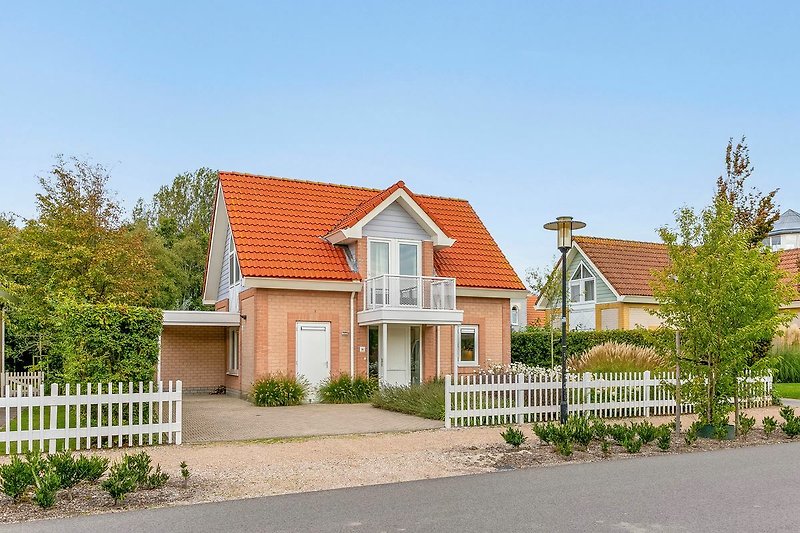 Charmantes Landhaus mit Garten, Zaun und blühenden Pflanzen.